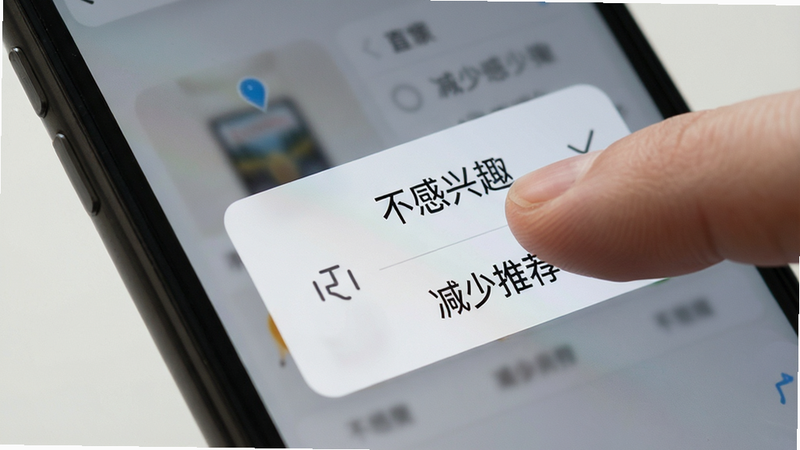 用户操作手机进行“不感兴趣”反馈的示意图,主体为手指点击屏幕的局部特写,布局聚焦于交互动作,排版简洁,风格写实,细节展示弹窗选项“不感兴趣”,画质逼真,干净,无多余元素,文字“减少推荐”清晰可见