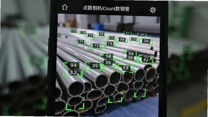 特写镜头,一部手机屏幕显示'点数相机iCount数钢管'的界面,屏幕上有一排整齐排列的金属钢管,每个钢管上方都有绿色的识别框和数字编号,背景虚化,突出屏幕内容,科技感强,清晰锐利,无水印