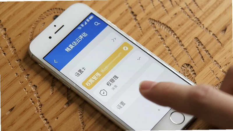 一部白色智能手机放在木质桌面上,屏幕显示精真估云评估的设置界面,高亮显示