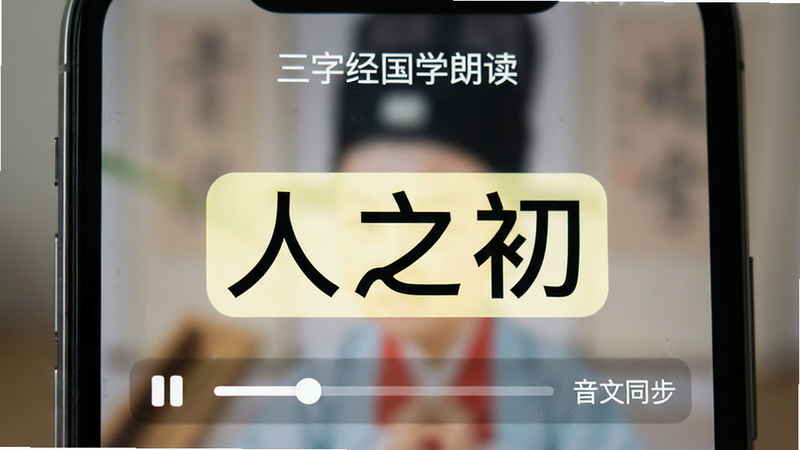 手机屏幕特写,显示“三字经国学朗读”界面,文字“人之初”高亮显示,背景虚化,布局聚焦于文本区域,排版整齐,风格清晰直观,细节包含播放进度指示器,画质高清,干净,无多余元素,文字“音文同步”