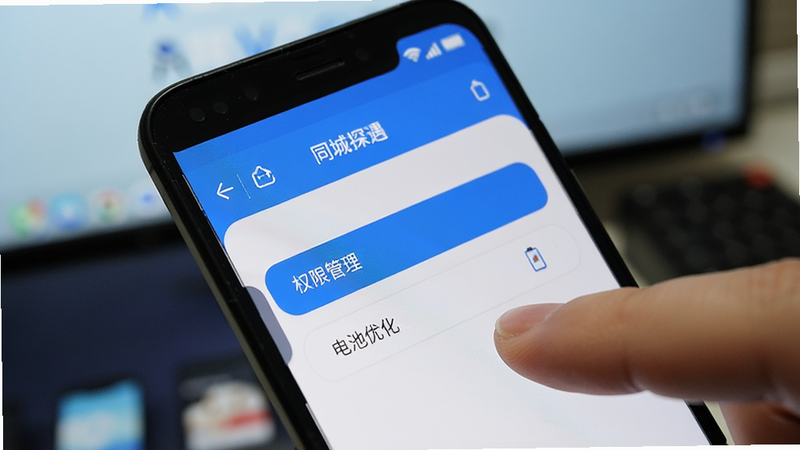 一部安卓手机的特写镜头,屏幕显示“同城探遇”APP的设置界面,高亮显示“权限管理”和“电池优化”选项,手指正在点击屏幕进行设置操作,背景为模糊的桌面壁纸,光线明亮,细节清晰,展现用户调整隐私与性能设置的场景,风格写实,无多余干扰元素