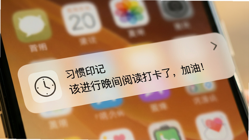 手机通知栏特写,背景模糊处理,突出一条来自“习惯印记”应用的通知消息。通知图标为简约的线条风格时钟图标,文字内容清晰显示“该进行晚间阅读打卡了,加油!”。整体色调温暖柔和,光线自然,营造出一种温馨、不具压迫感的提醒氛围。画质细腻,文字边缘锐利,无噪点,体现移动端通知界面的精致感