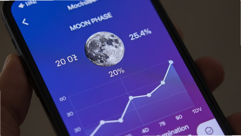 close-up view of a mobile app displaying the current moon phase with percentage illumination, simple graph lines, blue and purple gradient background, clear text labels