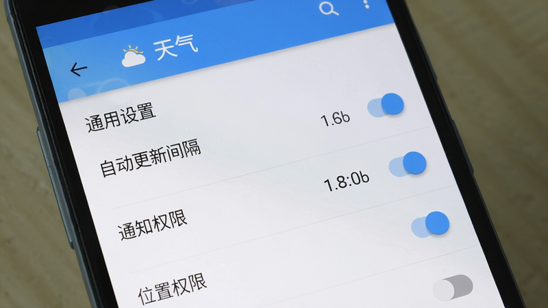 主体为手机屏幕上的“天气”应用设置界面,显示“通用设置”页面,包含“自动更新间隔”、“通知权限”、“位置权限”等开关选项。布局顶部有返回箭头和应用名称,中部是列表式设置项,每个选项右侧有开关按钮。风格是典型的安卓Material Design,白色背景,蓝色主题色,画质干净细腻。