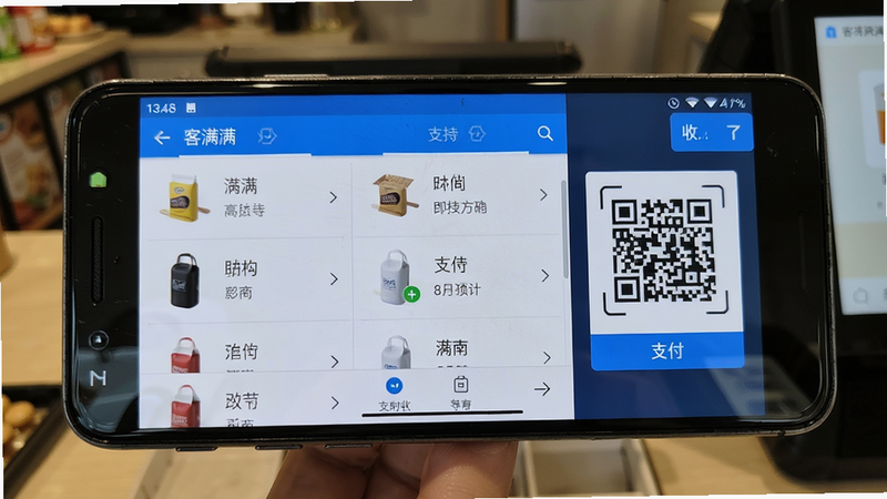 客满满在安卓手机上运行收银界面的实拍图,手机横屏显示商品列表和支付二维码;布局居中;风格真实场景;细节手机边框可见,屏幕内容清晰;画质高清干净,无多余元素