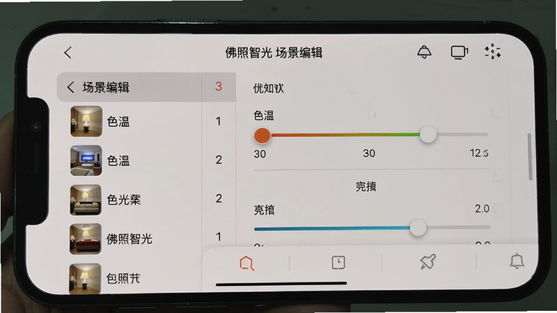 主体:手机运行佛照智光APP的实拍截图,布局:手机横屏显示,界面为场景编辑页面,排版:左侧为场景列表,右侧为灯具编辑区域,风格:真实手机拍摄,细节:屏幕上显示色温调节滑块和亮度条,画质:清晰,干净无多余元素,图片中文字“佛照智光 场景编辑”
