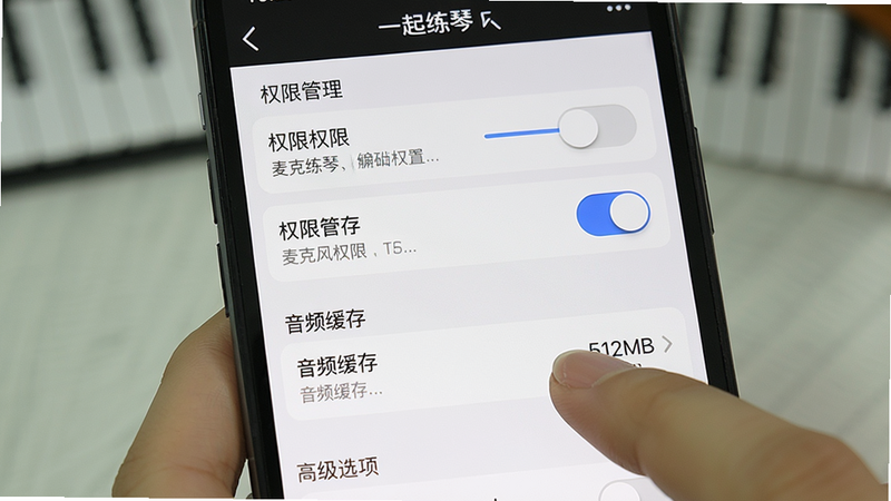 主体是手机竖屏界面,显示“一起练琴”设置页面的“权限管理”区域,麦克风权限开关为蓝色开启状态,下方有“音频缓存”选项,用户正用手指点击“512MB”选项。布局从上到下依次为权限列表、缓存设置、高级选项,风格为系统设置UI写实风,细节包括选项右侧的滑块和文字说明,画质清晰干净,无多余元素。