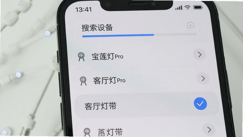 手机屏幕显示宝莲灯pro的蓝牙配对界面,顶部有“搜索设备”进度条,下方列出已发现的灯带名称,其中一个高亮显示“客厅灯带”并带有蓝色对勾图标,背景简洁,配色清爽,画质干净