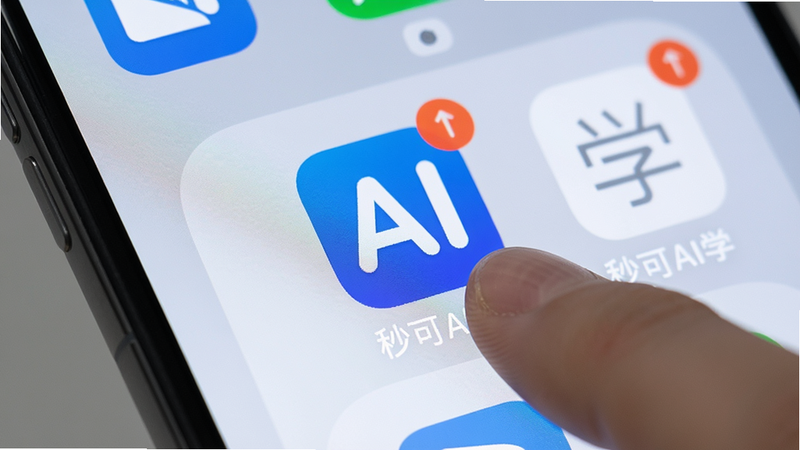 一张展示手机桌面秒可AI学图标的图片,主体为智能手机屏幕,桌面背景简洁,应用图标为蓝色底白色AI字母,周围有通知角标,手指正在点击图标,画质高清,风格真实摄影,无多余元素,文字“秒可AI学”出现在图标下方