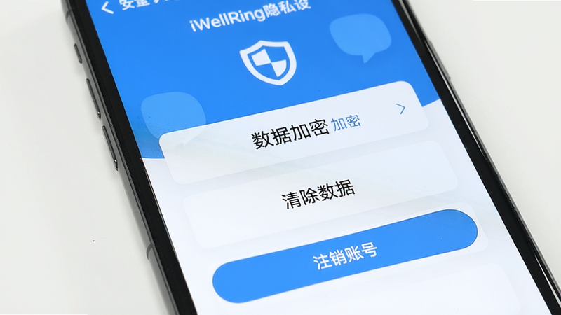 主体:手机屏幕显示iWellRing隐私设置页面,有“数据加密”、“清除数据”、“注销账号”按钮。布局:卡片式列表,顶部有盾牌图标。风格:简洁安全蓝配色。细节:文字清晰,“加密”等字样可见。画质:干净无多余元素。