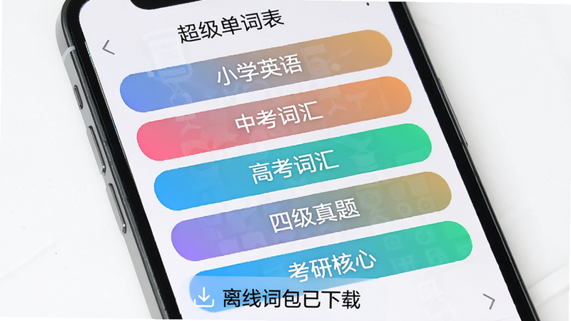 手机屏幕显示“超级单词表”词库列表,从上到下排列“小学英语”、“中考词汇”、“高考词汇”、“四级真题”、“考研核心”等标签,标签背景为渐变色,手机下方有“离线词包已下载”提示,整体风格清爽明亮。