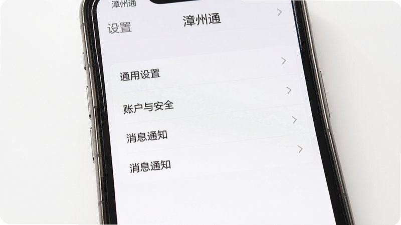 手机屏幕显示漳州通APP的“设置”页面,主体为“通用设置”“账户与安全”“消息通知”等选项列表,背景为白色,风格简洁清晰,画质高清,干净,屏幕上方有“漳州通”标题。