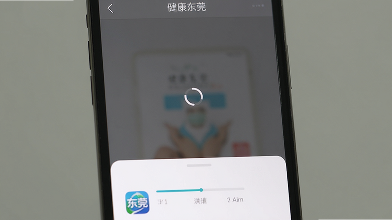 主体为手机屏幕显示“健康东莞”APP启动后停在加载页面,中央有旋转的加载圆圈,底部为白色背景,风格简洁,细节包括进度条、应用图标,画质清晰,无多余元素,屏幕上方显示“健康东莞”。