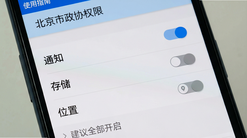 主体:手机屏幕展示“使用指南”中的权限设置界面,显示“通知”“存储”“位置”三个权限开关。布局:列表式排列,每个开关右侧有滑块。排版:权限名称加粗,开关状态用蓝色/灰色表示。风格:Android系统标准设置风格。细节:上方有“北京市政协权限”标题,下方有“建议全部开启”提示文字。画质:干净,无多余元素。