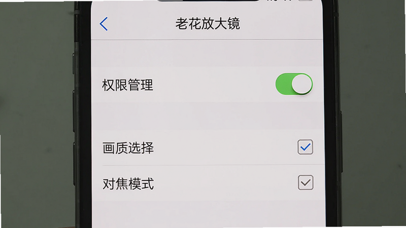 主体为手机屏幕上显示“老花放大镜”设置界面,包含“权限管理”“画质选择”“对焦模式”等选项。布局:设置列表从上到下排列,顶部有返回箭头和标题。风格系统原生UI,细节包括开关滑块、复选框,画质干净,无多余元素,图片中文字需为中文。