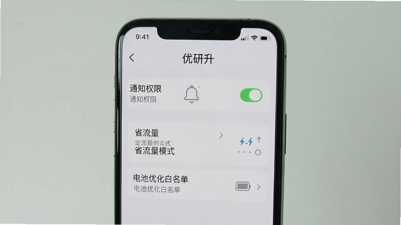 一张手机截图展示优研升app的设置页面,包含“通知权限”、“省流量模式”、“电池优化白名单”等选项,背景为灰白色,界面简洁,文字清晰,手机屏幕居中,周围无杂乱元素,画质高清,干净明亮