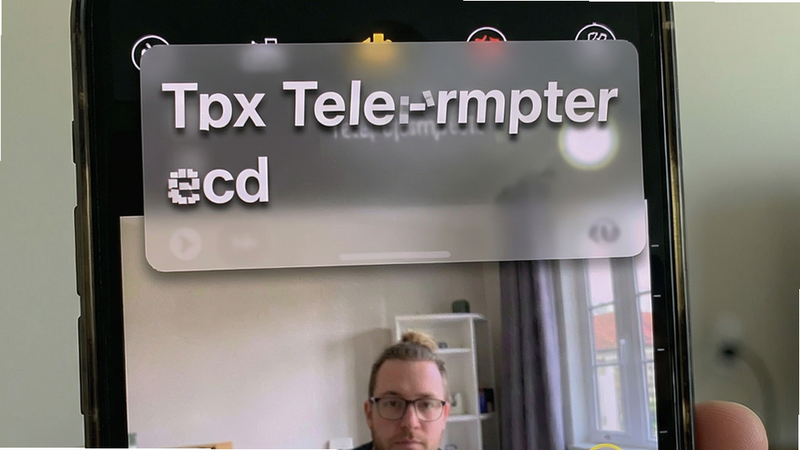 手机屏幕上同时显示相机录制界面和一个半透明的Tdx Teleprompter悬浮提词窗,提词文字清晰可读。布局为相机画面占大部分,悬浮窗位于上方三分之一处。排版自然融合,风格写实。细节包括悬浮窗的半透明效果和文字边缘的阴影处理。画质清晰,干净无多余元素。