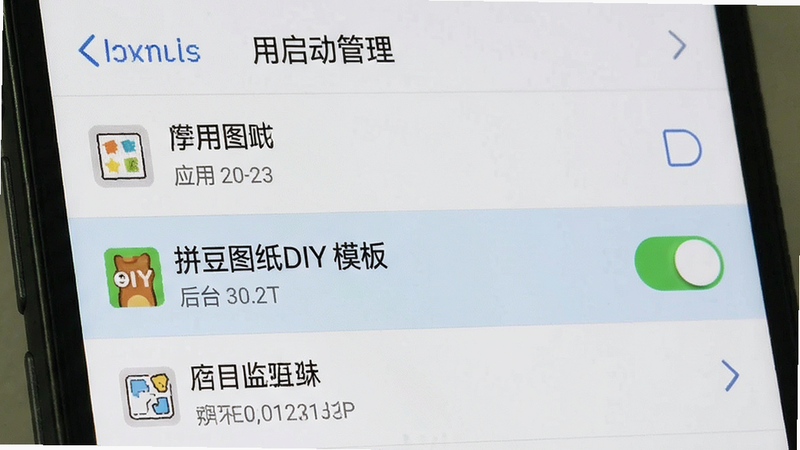 主体为手机设置界面截图,显示“应用启动管理”列表,高亮显示“拼豆图纸DIY模板”及其后台运行开关,布局为列表式,风格为系统原生UI,细节清晰可见,画质标准,干净无多余元素