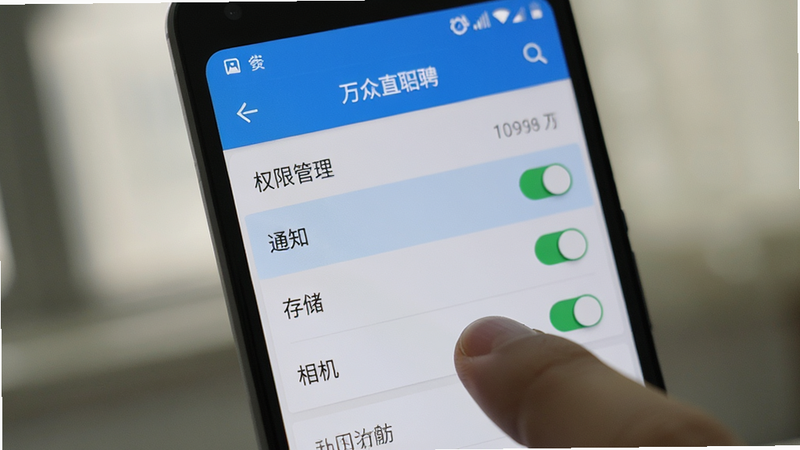 主体为安卓手机屏幕显示万众直聘APP的设置界面,布局聚焦于'权限管理'选项,高亮显示'通知'、'存储'、'相机'权限开关,风格写实,细节处有手指点击动作,画质清晰,强调权限配置,背景虚化