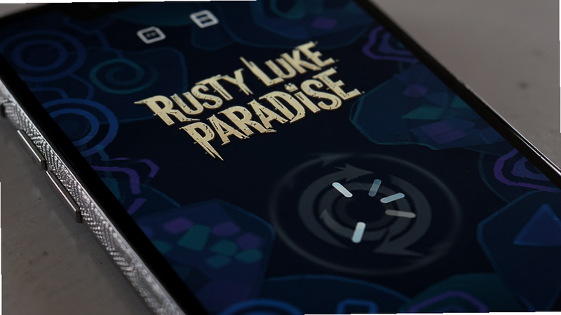 手机屏幕特写,显示 Rusty Lake Paradise 游戏加载界面,背景为深色抽象图案,前景有一个旋转的加载图标。画面干净简洁,突出手机边框的质感,光影柔和,现代科技风格,无多余界面元素