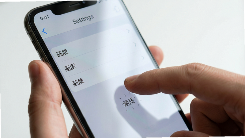 主体为一只手拿着智能手机,屏幕上显示设置界面,手指正在点击“画质”选项,布局特写,排版简洁,风格为写实摄影风,细节处有屏幕反光,画质清晰,干净背景,文字包含