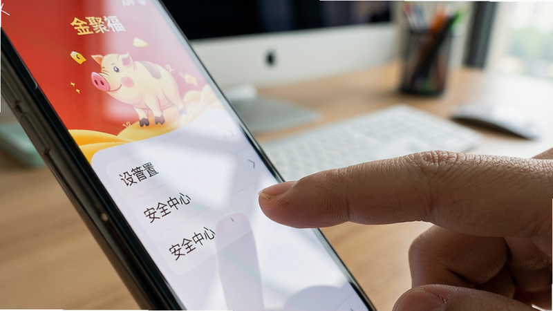 主体为手机侧边视角,布局为手机屏幕亮起显示金猪聚福APP的设置页面,手指正在点击“安全中心”选项,背景为模糊的办公桌场景,风格为写实摄影风,细节处有屏幕反光和手指纹理,画质高清,干净无杂物,突出操作细节
