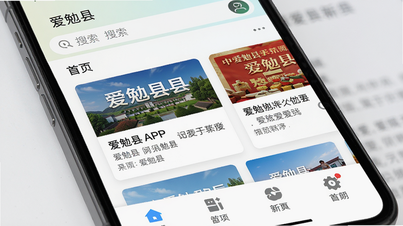 主体为手机屏幕界面,显示爱勉县APP首页,布局清晰,顶部有搜索栏,中部为新闻卡片,底部为功能图标,排版整洁,风格简约现代,细节丰富,画质高清,干净无多余元素,文字包含