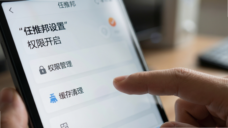 主体为任推邦设置界面特写,布局聚焦于“权限管理”和“缓存清理”选项,背景模糊处理以突出前景。风格为写实摄影风,光线柔和,细节处展示手指点击屏幕的动作,画质高清,干净,无多余元素,文字加引号“任推邦设置”“权限开启”