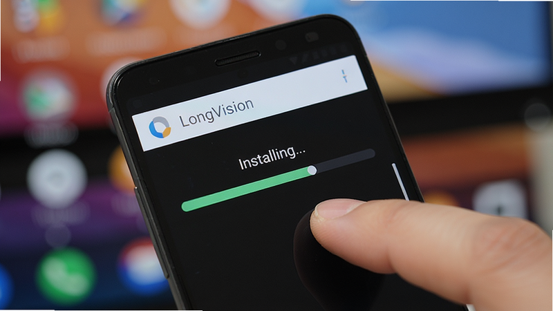 主体为一部安卓手机正在安装 LongVision 应用,屏幕上显示安装进度条,背景为模糊的桌面壁纸,布局为近景特写,风格为写实摄影,细节展示手指点击屏幕的动作,文字“Installing...”在进度条上方,画质高清,干净,无多余元素