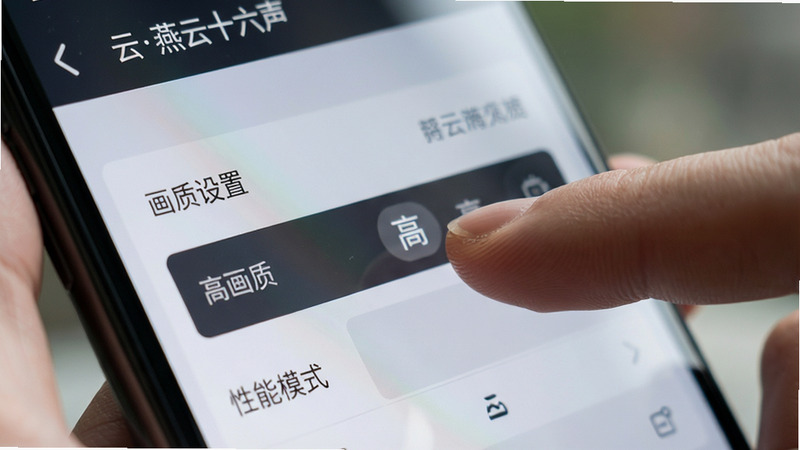 手机屏幕特写,显示《云燕云十六声》的设置界面,焦点在“画质设置”和“性能模式”选项上。手指正在点击“高”画质选项。背景模糊,突出操作细节。布局紧凑,UI元素清晰。风格写实摄影风,光影柔和。细节展示屏幕反光与手指触感。画质高清,干净,无多余元素,文字“高画质”清晰可辨。