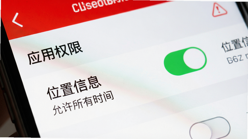 主体为手机设置界面特写,布局聚焦于“应用权限”列表,风格为警示性红白配色,细节包含“位置信息”开关处于开启状态,文字标注“允许所有时间”,画质清晰,无多余元素