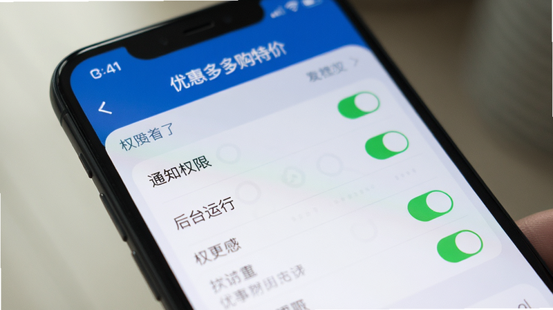 主体为一部智能手机特写,屏幕显示“优惠多多购特价”的设置界面,布局聚焦于权限开关列表,排版清晰,风格为写实摄影结合UI设计,细节展示“通知权限”、“后台运行”等选项被高亮勾选,画质真实自然,光线柔和,背景虚化以突出手机主体,无多余杂物