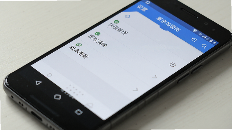 主体为一部安卓手机,屏幕显示“爱亲加盟商”APP的设置页面,布局为列表菜单,包含权限管理、缓存清除、版本更新等选项,排版清晰,风格为系统设置界面风,细节真实,高清画质,干净,文字包含