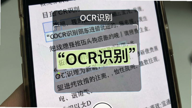 主体为手机摄像头界面,正在拍摄一份纸质文档,屏幕上方叠加OCR识别框,布局突出识别区域,排版简洁,风格写实摄影风,细节展示文字被高亮框选,画质锐利,干净,无多余元素,文字“OCR识别”加引号