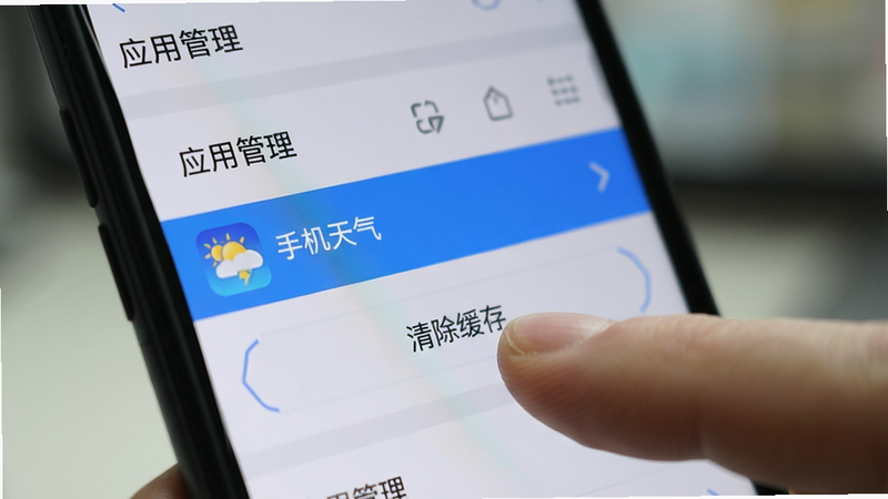 主体为手机设置界面截图,显示“应用管理”列表,高亮显示“手机天气”应用,下方有“清除缓存”按钮被手指点击,背景模糊处理,焦点集中在按钮上,风格写实,高清细节,操作演示感强