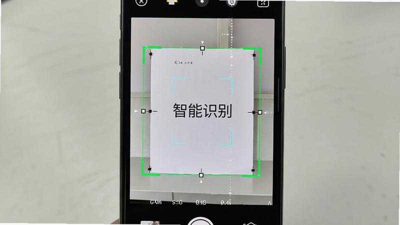 主体为手机相机界面,展示自动裁剪功能,布局中屏幕中央有一个绿色的四边形选区框住一张白色A4纸,排版直观,风格专业,细节显示算法正在计算边缘坐标,画质高清,干净,无多余装饰,文字“智能识别”