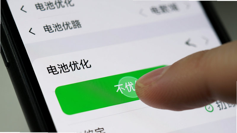 主体为手机设置界面特写,布局聚焦于“电池优化”选项,手指正在点击“不优化”按钮,按钮呈高亮绿色,背景为模糊的手机设置菜单,风格为写实UI截图风格,细节展示手指点击的交互反馈,画质清晰,无多余图标干扰。