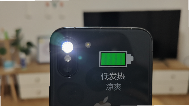 手机背面视角,闪光灯处于开启状态,旁边有一个电池图标显示绿色电量,背景为模糊的室内环境,主体为手机背部,布局平衡,排版整洁,风格为生活化实拍感,细节展示温度标识为凉爽,画质真实,无过度曝光,文字标注“低发热”