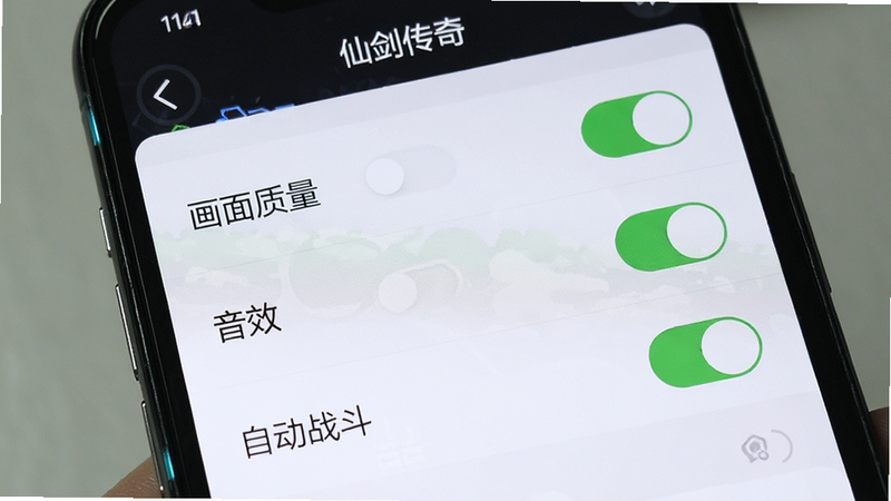 手机屏幕特写,主体为“仙剑传奇”游戏的设置界面,布局为列表形式,显示“画面质量”、“音效”、“自动战斗”等选项,排版为垂直列表,风格为简洁现代,细节显示开关按钮处于开启状态,画质清晰,UI字体清晰,无其他图标,突出设置便捷性