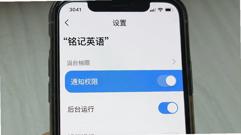 主体为手机屏幕界面,展示“铭记英语”APP的设置页面,布局为列表式,背景为白色,高亮显示“通知权限”和“后台运行”选项,风格简洁现代,细节包含开关按钮的选中状态,画质清晰,干净,文字“设置”加引号