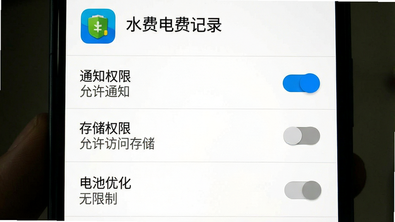 主体为手机设置界面截图,展示“水费电费记录”APP的权限管理页面,布局为垂直列表,顶部是应用图标和名称,下方依次是“通知权限”、“存储权限”、“电池优化”开关,排版标准安卓风格,风格为系统原生UI,细节包括开关的蓝色激活状态和灰色的未激活状态,文字包含“允许通知”、“允许访问存储”、“无限制”,画质清晰,背景为白色,无多余元素