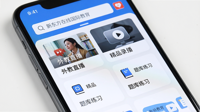 主体为一部现代智能手机,屏幕显示“新东方在线国际教育”App主界面,布局清晰,顶部为搜索栏,中部展示“外教直播”、“精品录播”、“题库练习”等模块卡片,排版整齐,风格简约现代,细节包含清晰的图标和文字,画质高清,干净,无多余元素