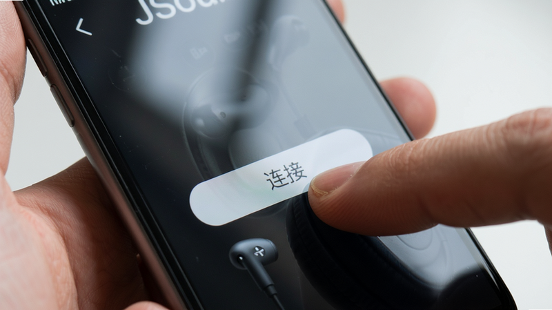 手持智能手机操作 JSoul APP 连接耳机的场景,主体为手指点击“连接”按钮,布局特写,排版聚焦屏幕中心,风格写实摄影,细节展示屏幕反光与手指纹理,画质高清,干净,无多余元素
