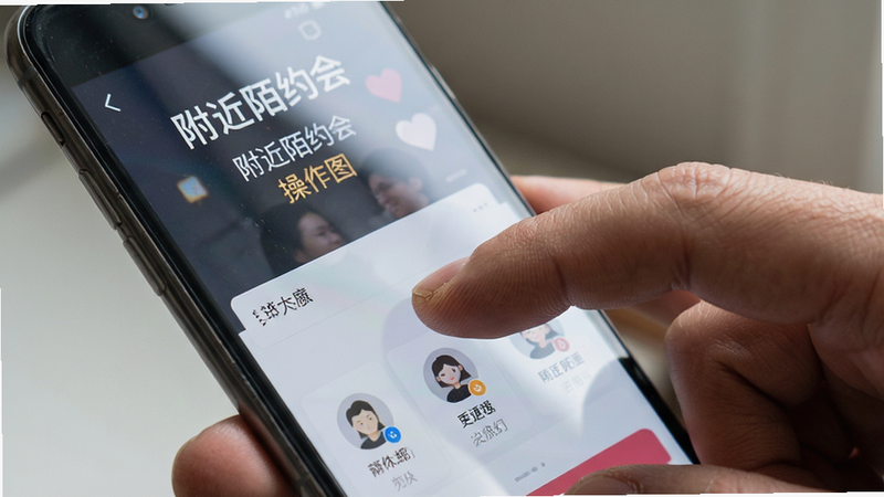 主体为手机手持示意图,屏幕显示“附近陌约会”应用界面,布局为特写镜头,手指点击屏幕动作,排版聚焦于屏幕内容,风格生活化写实,细节包含屏幕反光与手部纹理,画质逼真,干净,无多余元素,alt=