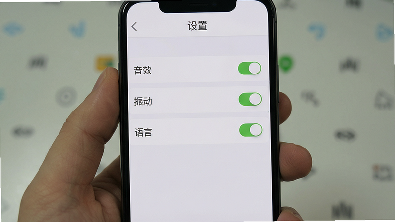 主体为手机屏幕显示游戏设置界面,布局为列表形式,显示音效、振动、语言等选项,背景为浅灰色,风格为简约UI,细节处有开关按钮,画质清晰,干净,无多余元素,文字“设置”在顶部