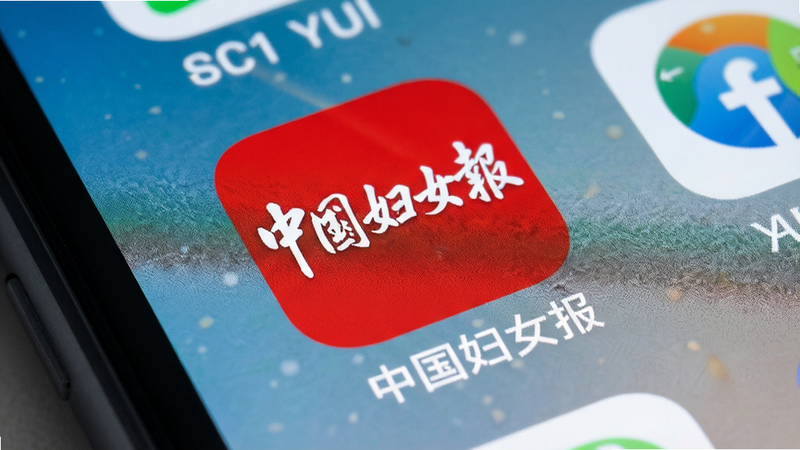 手机桌面特写,显示“中国妇女报”APP图标,红色背景白色文字,周围无其他应用干扰,光线均匀,高清摄影风格,细节锐利