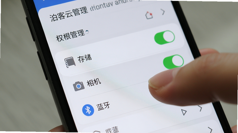 泊客云安卓手机设置界面特写,主体为手机屏幕显示权限管理页面,高亮显示“存储”、“相机”、“蓝牙”权限为开启状态,布局简洁,风格写实,细节展现手指点击操作的动作,画质清晰,无多余文字干扰