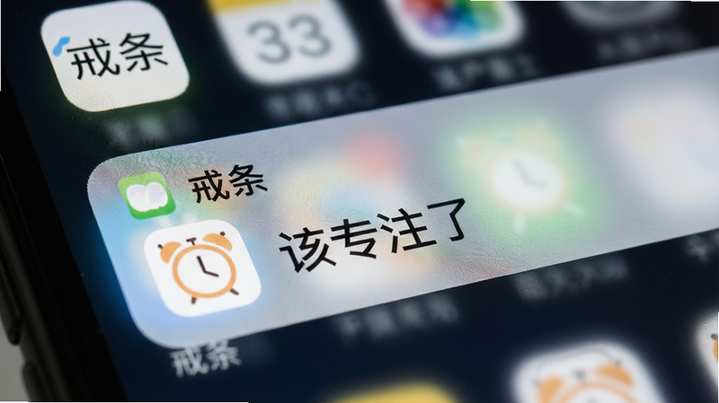 主体为手机通知栏特写,显示一条来自“戒条”的通知,内容包含一个温和的闹钟图标和“该专注了”的文字提示,背景模糊处理以突出通知内容,布局位于屏幕顶部,排版清晰易读,风格为写实摄影与数字界面结合,细节展现屏幕反光与像素质感,画质细腻,干净无杂乱信息,文字“戒条”在应用图标处可见