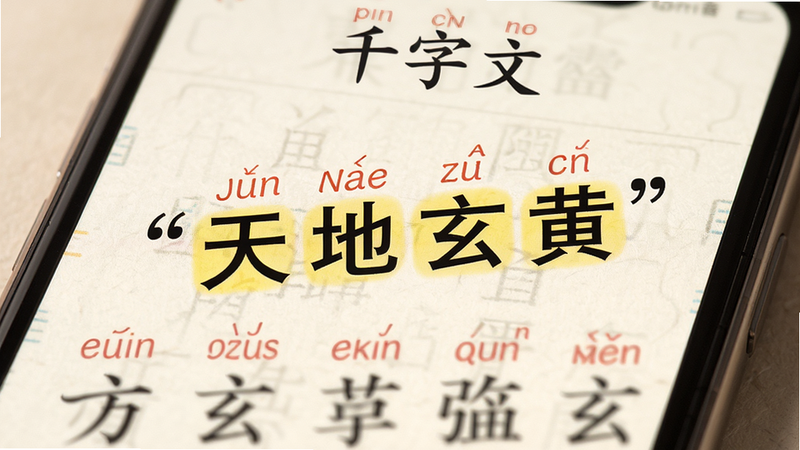 主体为手机屏幕特写,显示《千字文》文本页面,每个汉字上方标注红色拼音,部分文字高亮显示,背景为米白色宣纸质感,布局紧凑有序,风格为教育科技风,细节处有柔和的光影效果,画质清晰,干净,无多余元素,文字加引号“天地玄黄”