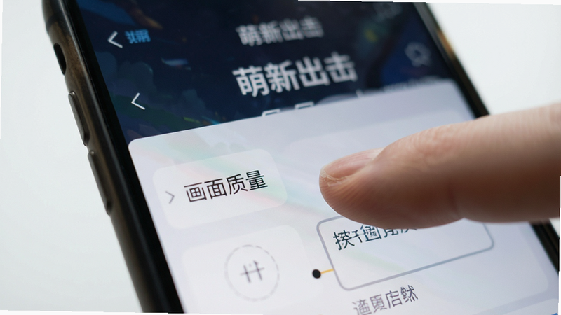 一张手机屏幕特写图,显示“萌新出击”的设置界面,手指正在点击“画面质量”选项,背景模糊,焦点集中在屏幕文字上,风格写实,布局清晰,细节逼真,画质高,干净背景